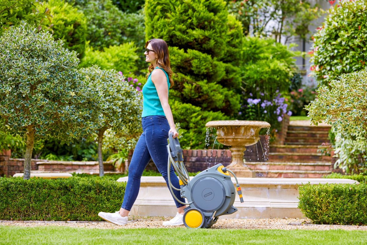 Un'immagine che mostra una giovane donna in jeans e top verde che passeggia nel suo giardino con l'Auto Reel Mobile.