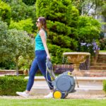 Un'immagine che mostra una giovane donna in jeans e top verde che passeggia nel suo giardino con l'Auto Reel Mobile.