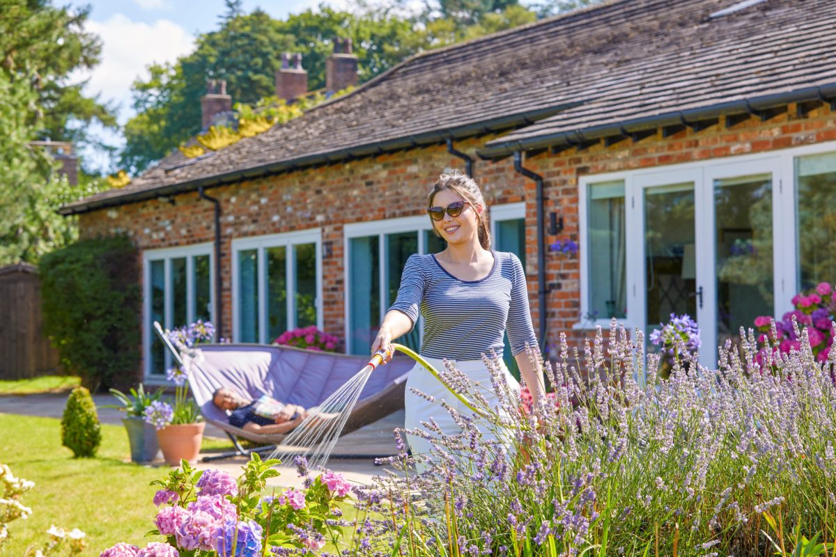 Una signora con un top a righe innaffia le piante nel giardino sul retro utilizzando il tubo Hozelock Ultimate in PVC fino al 75%.